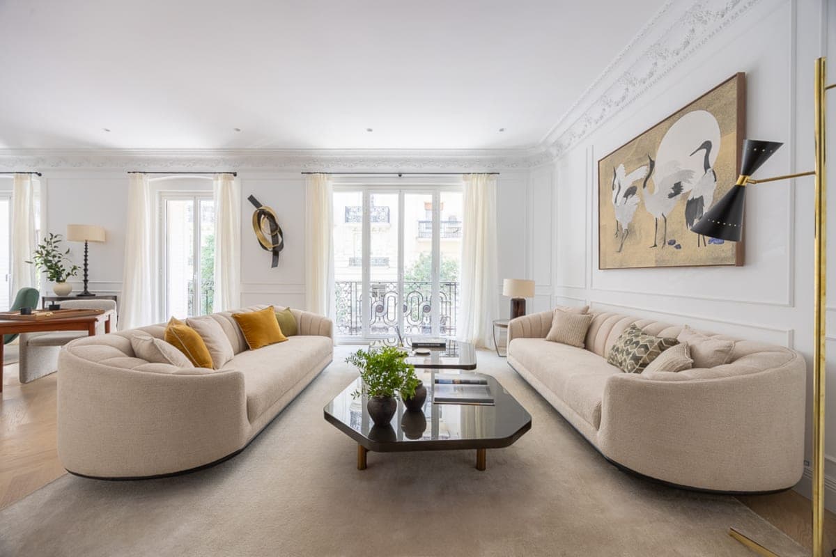 Salón clásico con sofás curvos cremas, balcón de hierro fundido y obra sobre fondo dorado en propiedad de Núñez de Balboa, barrio de Salamanca, Madrid — Coco House