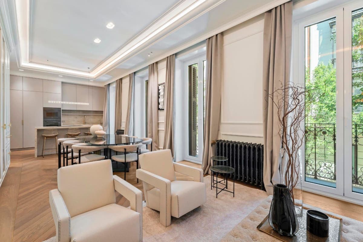 Salón con sillones cremas y mesa de comedor junto a balcón de hierro fundido en piso reformado a estrenar en Conde de Aranda, barrio de Salamanca, Madrid — Coco House