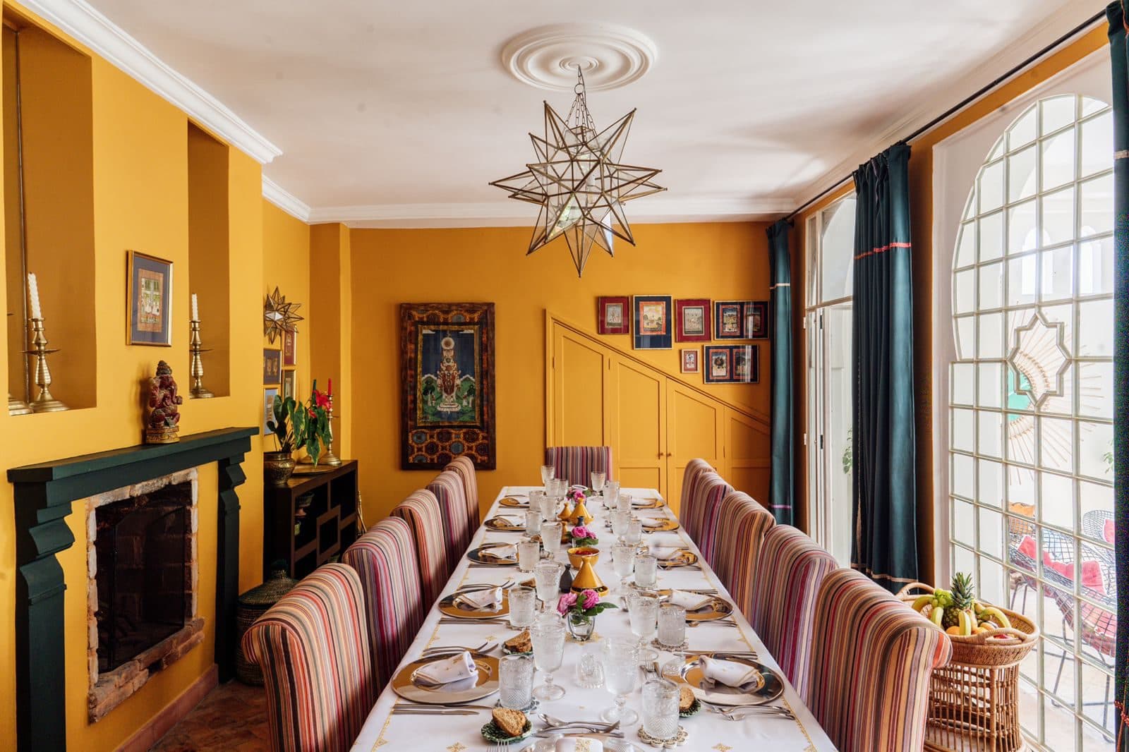 Dar Chal — Tánger, Marruecos Comedor de Dar Chal con mesa larga para doce, lámpara de araña y paredes en ocre — villa de lujo en Tánger (Coco House)
