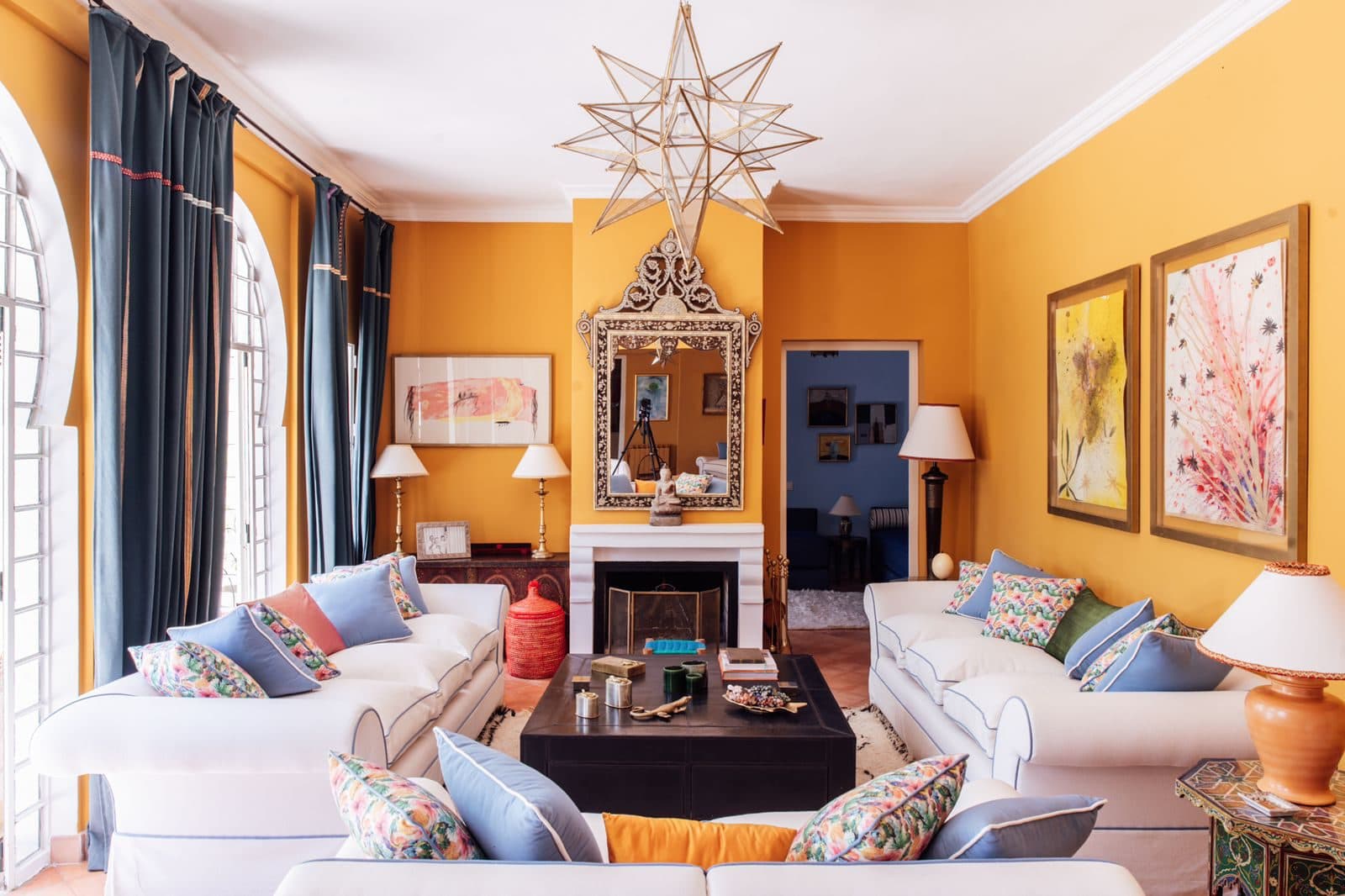 Dar Chal — Tánger, Marruecos Salón con chimenea, farol de estrella marroquí y sofás blancos bajo cortinas azules — Dar Chal, Tánger (Coco House)