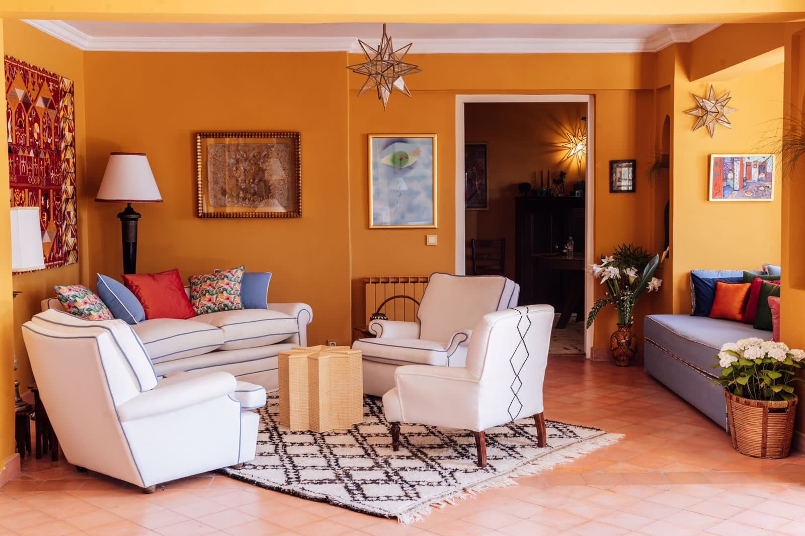 Dar Chal — Tánger, Marruecos Salón principal en ocre con sofás blancos, suelo de barro cocido y arcos hacia el jardín — Dar Chal, Tánger (Coco House)