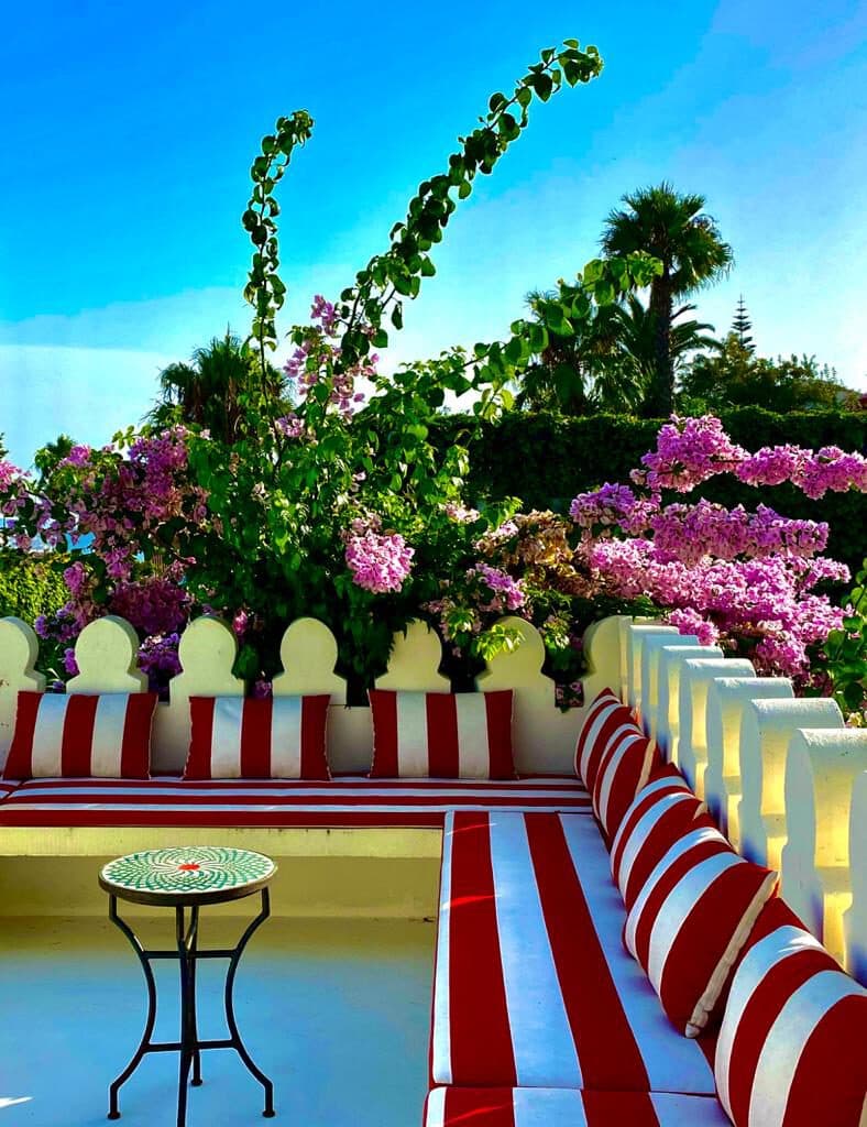 Dar Chal — Tánger, Marruecos Terraza con bancos tapizados a rayas rojas y blancas, buganvilla y parapeto almenado — Dar Chal, Tánger (Coco House)